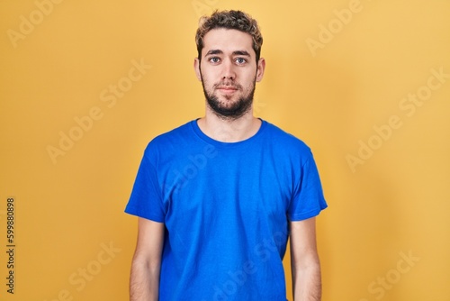 Hispanic man with beard standing over yellow background relaxed with serious expression on face. simple and natural looking at the camera.