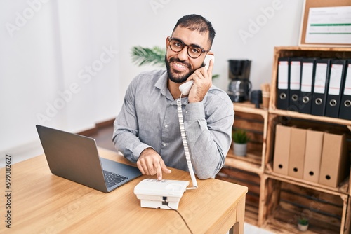 Young hispanic man business worker talking on telephone using laptop at office