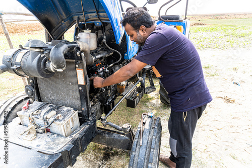 Open tractor hood, engine. Farmer mechanic repairing blue tractor engine. Combine machine service