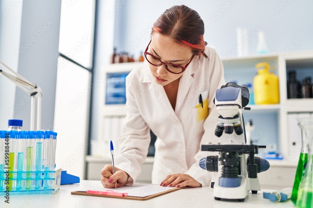 Young caucasian woman scientist writing report working at laboratory Young caucasian woman scientist writing report working at laboratory