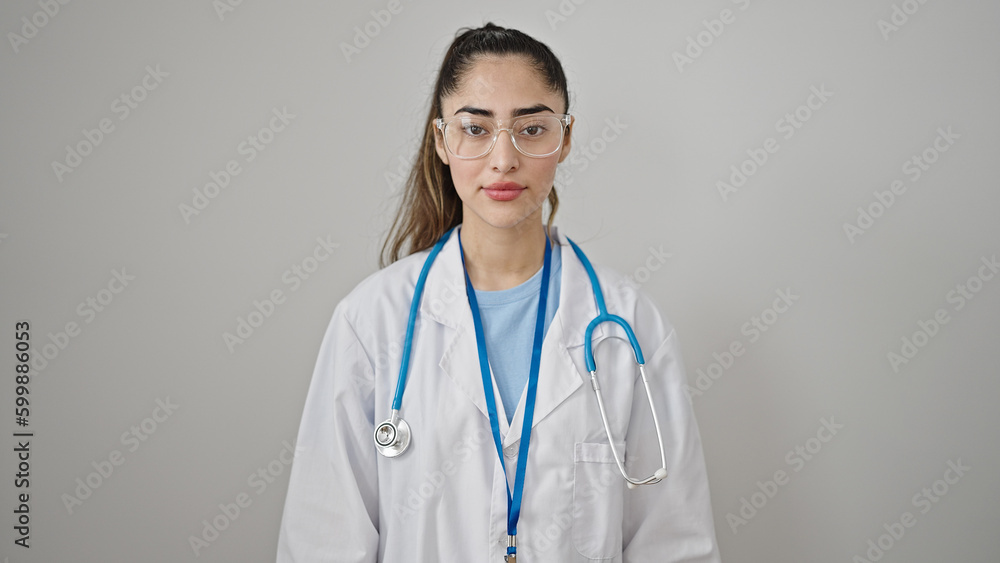Young beautiful hispanic woman doctor standing with serious expression over isolated white background