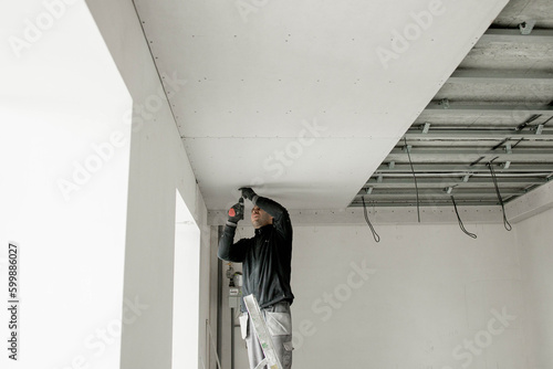 The worker attaches plasterboard on metal frame. Installation of ceiling photo