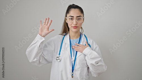 Young beautiful hispanic woman doctor making an oath with hand on chest over isolated white background
