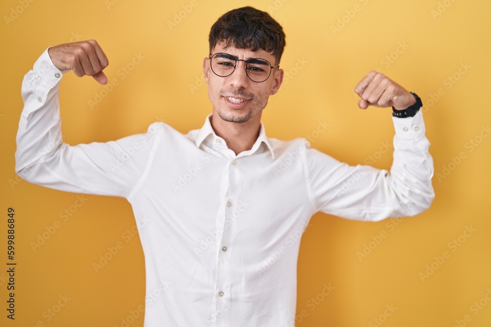 Fototapeta premium Young hispanic man standing over yellow background showing arms muscles smiling proud. fitness concept.