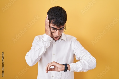 Young hispanic man standing over yellow background looking at the watch time worried, afraid of getting late © Krakenimages.com