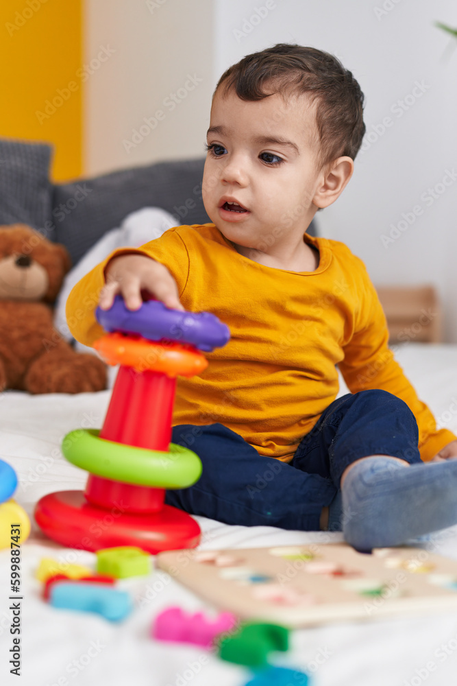 Adorable hispanic boy playing with hoops game sitting on bed at bedroom Adorable hispanic boy playing with hoops game sitting on bed at bedroom