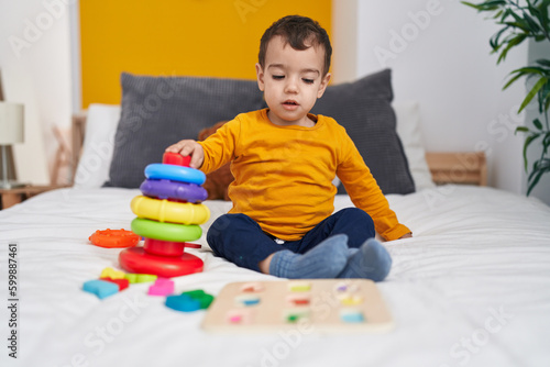 Adorable hispanic boy playing with hoops game sitting on bed at bedroom