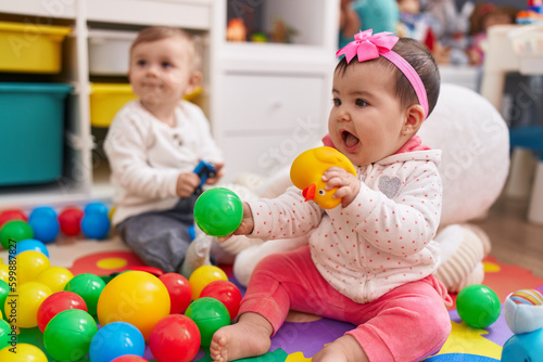Adorable boy and girl playing with balls sitting on floor at kindergarten