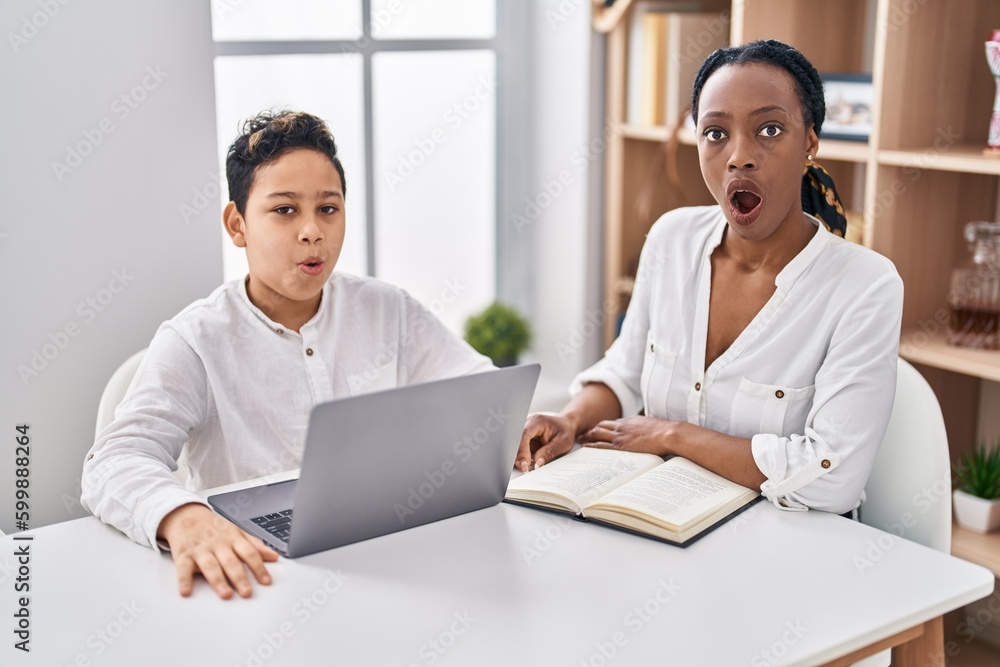 Young mother and son doing homework with laptop scared and amazed with open mouth for surprise, disbelief face Young mother and son doing homework with laptop scared and amazed with open mouth for surprise, disbelief face