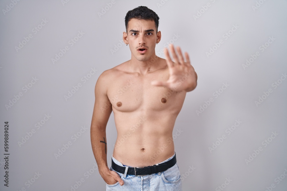 Handsome hispanic man standing shirtless doing stop gesture with hands palms, angry and frustration expression