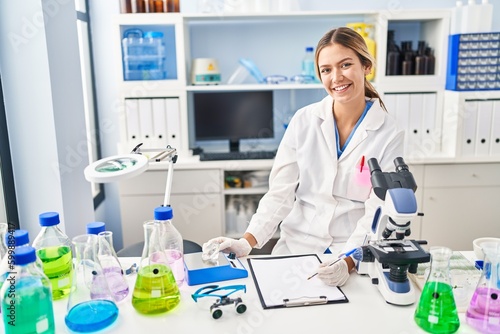 Young hispanic woman scientist weighing diamond writing report at laboratory