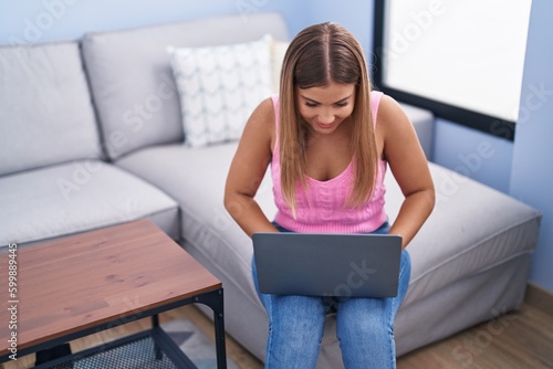 Young beautiful hispanic woman using laptop sitting on sofa at home