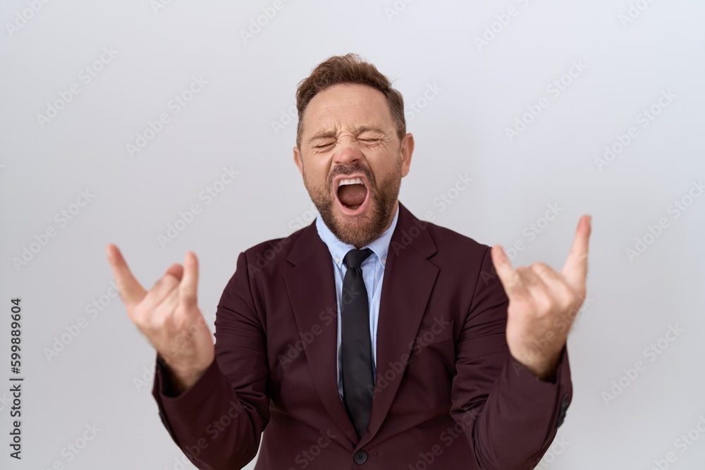 Middle age business man with beard wearing suit and tie shouting with crazy expression doing rock symbol with hands up. music star. heavy music concept. Middle age business man with beard wearing suit and tie shouting with crazy expression doing rock symbol with hands up. music star. heavy music concept.