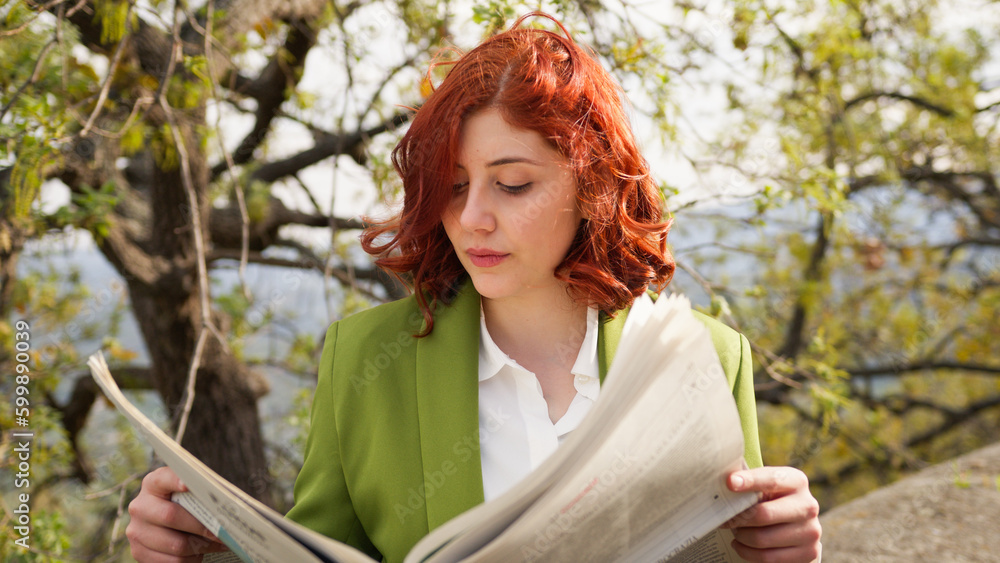 Naklejka premium Red hair businesswoman reading newspaper under the tree