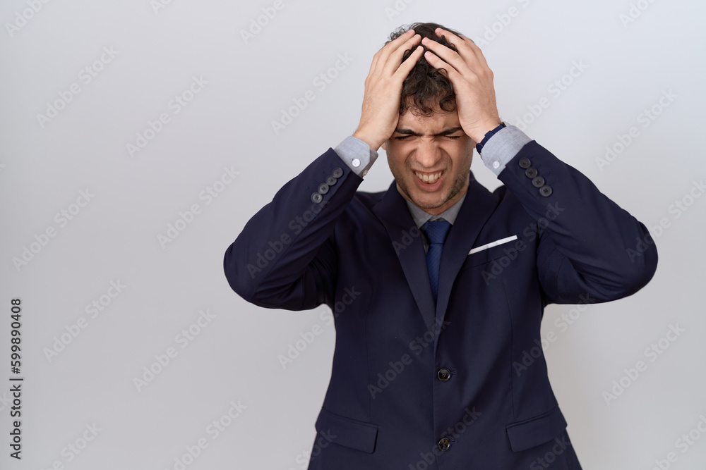 Young hispanic business man wearing suit and tie suffering from headache desperate and stressed because pain and migraine. hands on head. Young hispanic business man wearing suit and tie suffering from headache desperate and stressed because pain and migraine. hands on head.