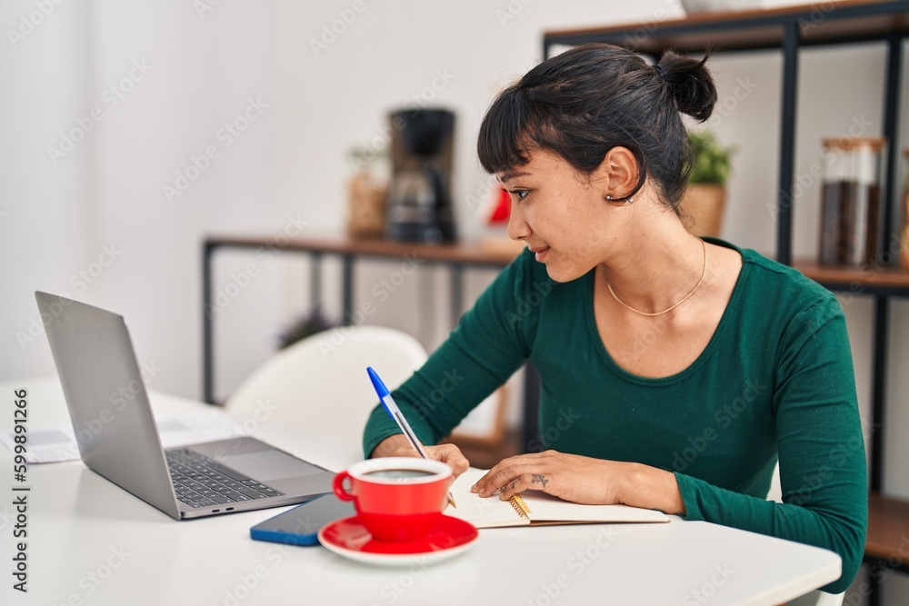 Young beautiful hispanic woman sitting on table studying at home Young beautiful hispanic woman sitting on table studying at home