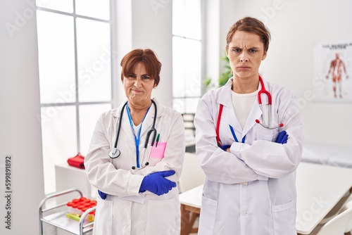 Two women wearing doctor uniform and stethoscope skeptic and nervous  disapproving expression on face with crossed arms. negative person.
