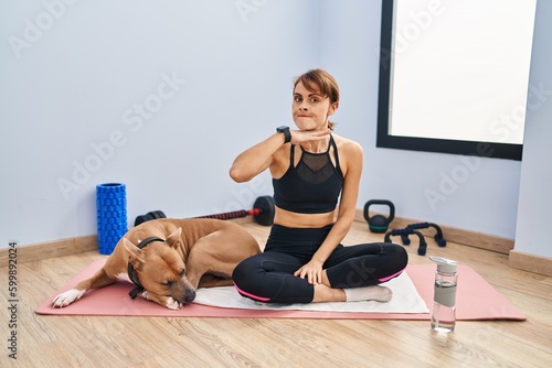 Young beautiful woman sitting on yoga mat cutting throat with hand as knife, threaten aggression with furious violence