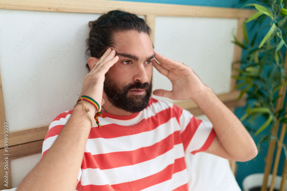 Young hispanic man sitting on bed suffering for headache at bedroom Young hispanic man sitting on bed suffering for headache at bedroom