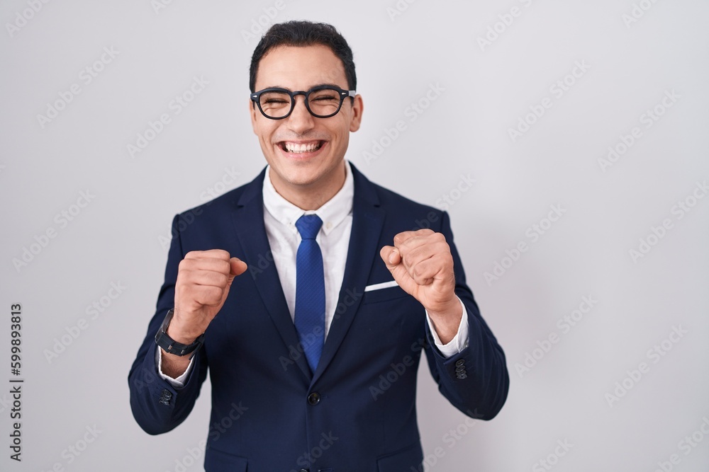 Young hispanic man wearing suit and tie excited for success with arms raised and eyes closed celebrating victory smiling. winner concept. Young hispanic man wearing suit and tie excited for success with arms raised and eyes closed celebrating victory smiling. winner concept.