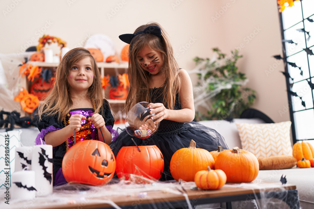 Adorable girls having halloween party putting candies in pumpkin basket at home