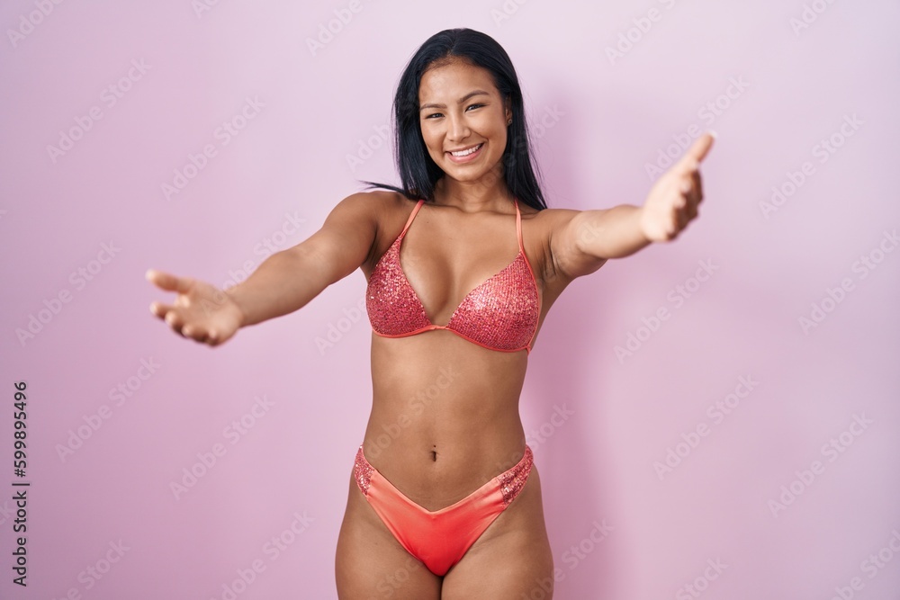 Hispanic woman wearing bikini looking at the camera smiling with open arms for hug. cheerful expression embracing happiness. Hispanic woman wearing bikini looking at the camera smiling with open arms for hug. cheerful expression embracing happiness.