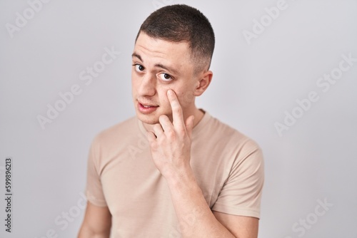 Young man standing over isolated background pointing to the eye watching you gesture, suspicious expression