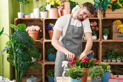 Young caucasian man florist talking on smartphone cutting plant at flower shop