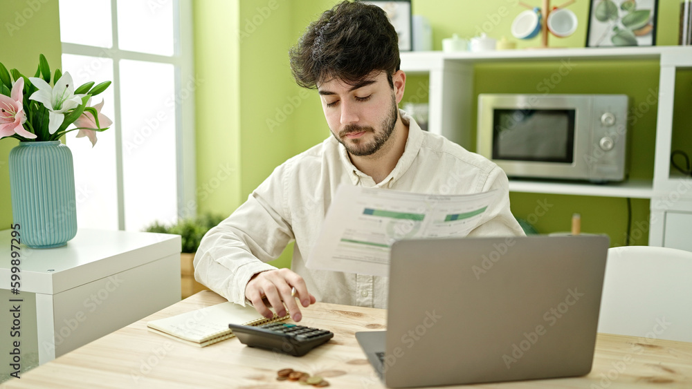 Young hispanic man sitting on table accounting at dinning room Young hispanic man sitting on table accounting at dinning room