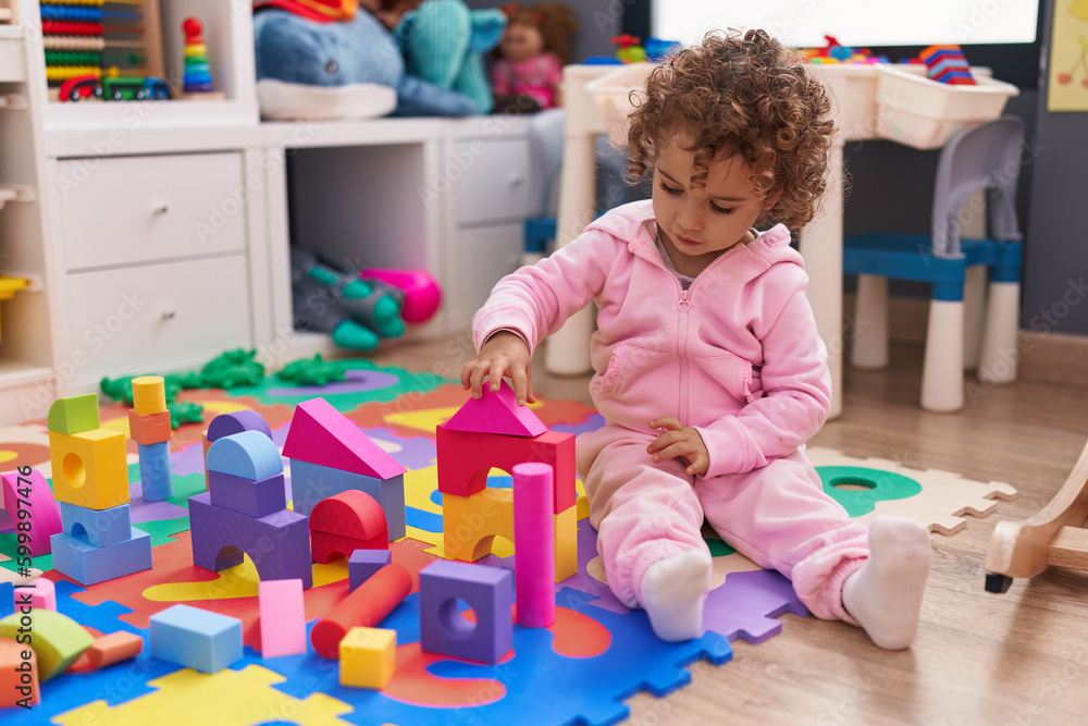 Fototapeta premium Adorable hispanic girl playing with construction blocks sitting on floor at kindergarten