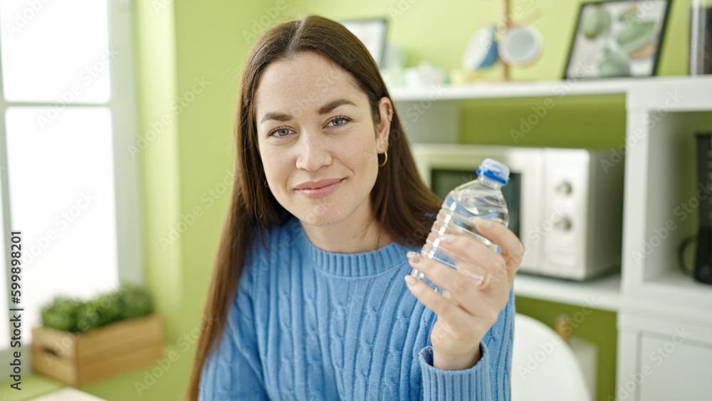Young caucasian woman smiling confident holding bottle of water sitting on table at dinning room Young caucasian woman smiling confident holding bottle of water sitting on table at dinning room