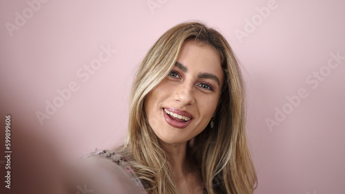 Young blonde woman smiling confident making selfie by camera over isolated pink background