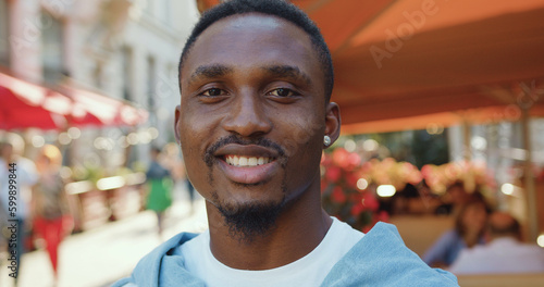 Likable smiling in good mood modern young african american looking at camera with lucky face near cozy street cafe in summertime,slow motion