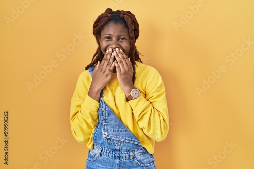 фотографія African woman standing over yellow background laughing and embarrassed giggle co