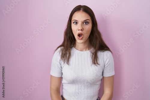 Young hispanic girl standing over pink background afraid and shocked with surprise and amazed expression, fear and excited face.