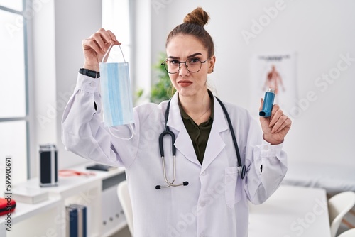 Young hispanic girl holding medical asthma inhaler at the clinic skeptic and nervous  frowning upset because of problem. negative person.