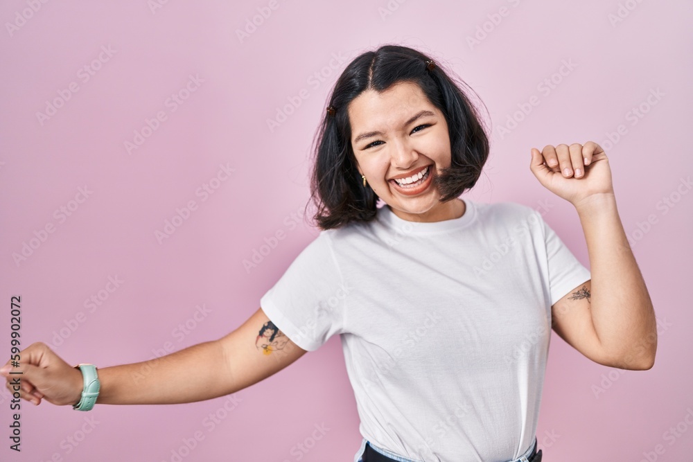 Young hispanic woman wearing casual white t shirt over pink background dancing happy and cheerful, smiling moving casual and confident listening to music Young hispanic woman wearing casual white t shirt over pink background dancing happy and cheerful, smiling moving casual and confident listening to music
