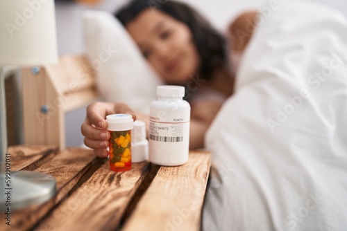 Young woman lying on bed holding pills bottle at bedroom