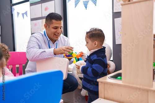 Hispanic man and boy playing with play kitchen standing at kindergarten