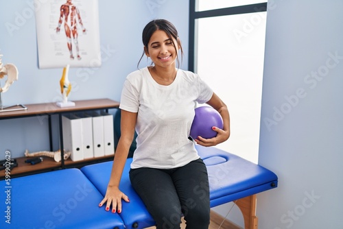 Young latin woman patient having rehab session holding ball at physiotherapy clinic