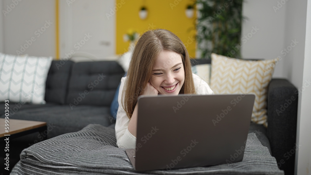 Young blonde woman using laptop lying on sofa at home Young blonde woman using laptop lying on sofa at home