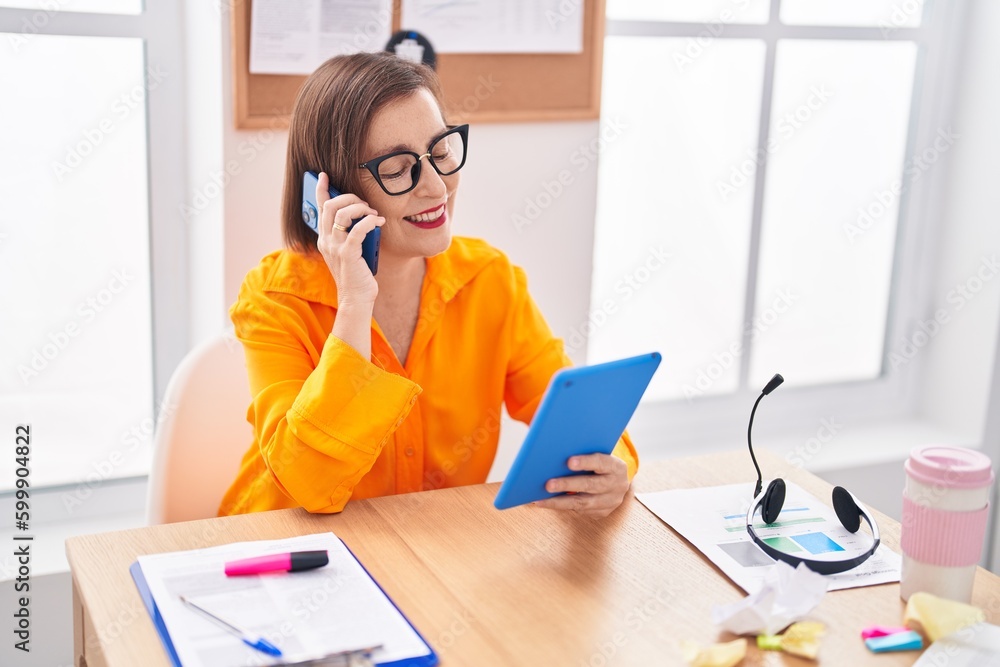 Middle age woman business worker talking on smartphone using touchpad at office Middle age woman business worker talking on smartphone using touchpad at office