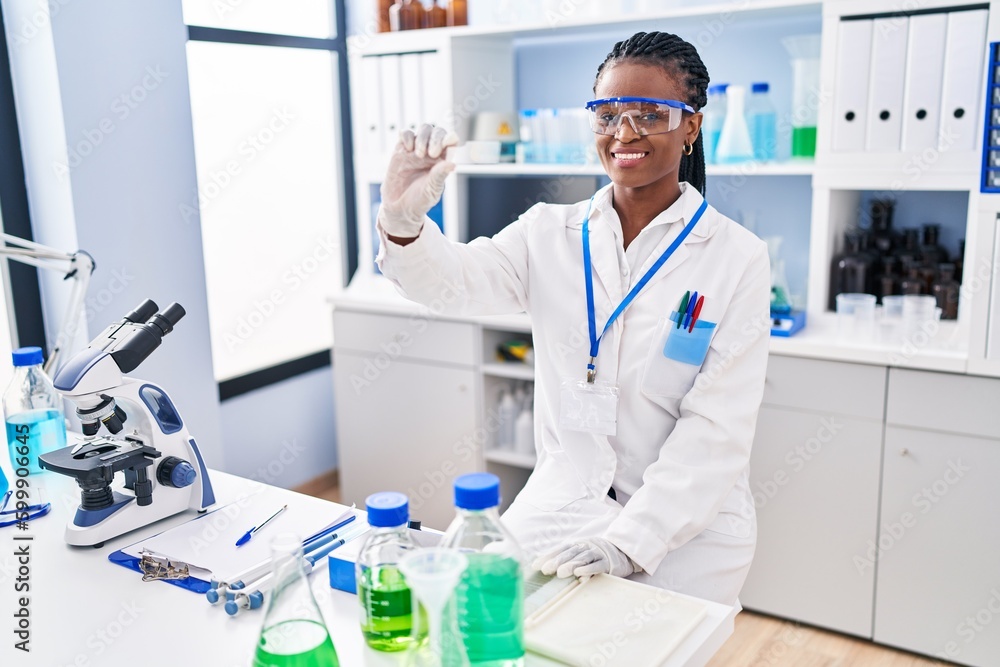 African american woman scientist smiling confident holding sample at laboratory