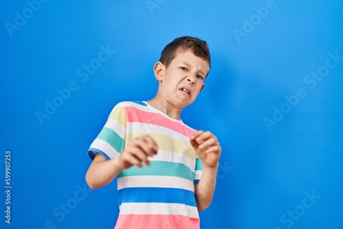Young caucasian kid standing over blue background disgusted expression, displeased and fearful doing disgust face because aversion reaction.
