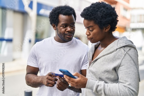 African american man and woman couple using smartphone and credit card at street