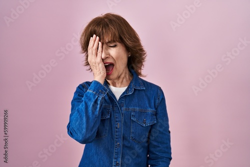 Middle age woman standing over pink background yawning tired covering half face, eye and mouth with hand. face hurts in pain. © Krakenimages.com