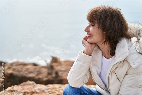 Middle age woman smiling confident sitting on the rock at seaside © Krakenimages.com