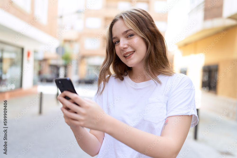 Fototapeta premium Young caucasian woman smiling confident using smartphone at street