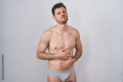 Young hispanic man standing shirtless wearing underware with hand on stomach because indigestion, painful illness feeling unwell. ache concept.