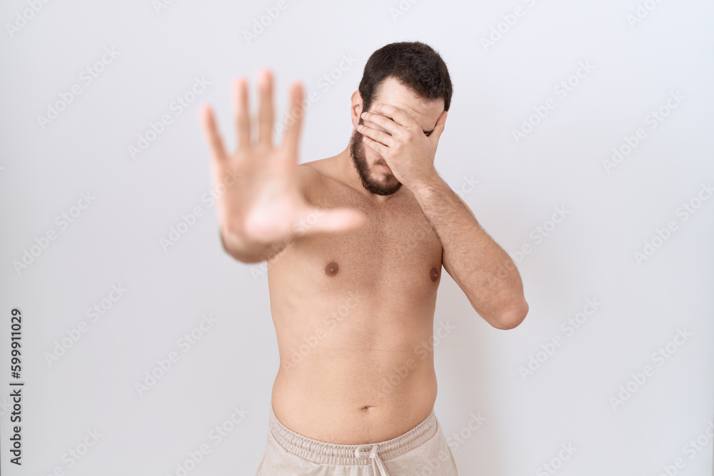Young hispanic man standing shirtless over white background covering eyes with hands and doing stop gesture with sad and fear expression. embarrassed and negative concept.